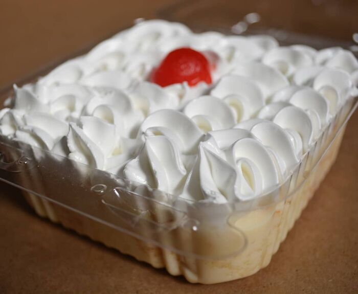 Christmas dessert with whipped cream topping and a cherry in a clear plastic container, showcasing festive treats from around the world.