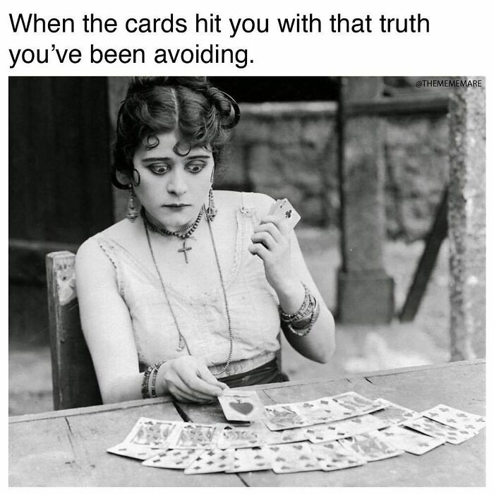 Woman with gothic style and dark makeup looking shocked while holding playing cards in a humorous goth meme about facing truth.