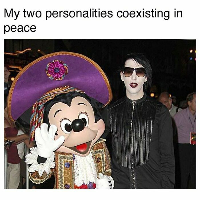 Person in goth attire with white makeup and sunglasses standing next to a person in a colorful Mickey Mouse costume, goth memes.