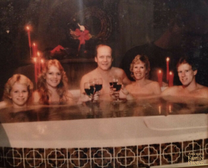 Family enjoying an awkward Christmas photo in a hot tub with candles and holiday decorations in the background.