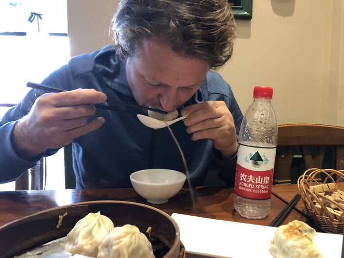 Man using chopsticks and spoon to eat soup dumplings in a funny, interesting, and weird pic taken at the perfect time