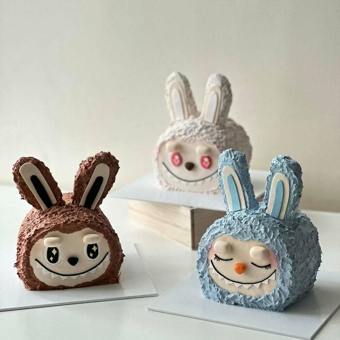 Three masterfully crafted cakes shaped like smiling bunny faces with textured icing in brown, blue, and white.