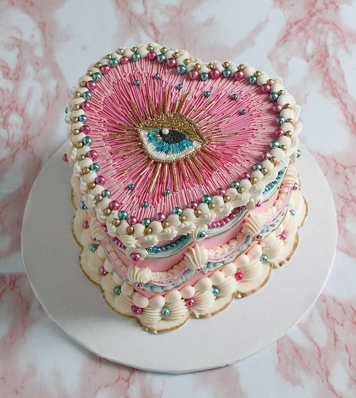 Heart-shaped masterfully crafted cake decorated with intricate pink icing and colorful edible pearls on a white board.