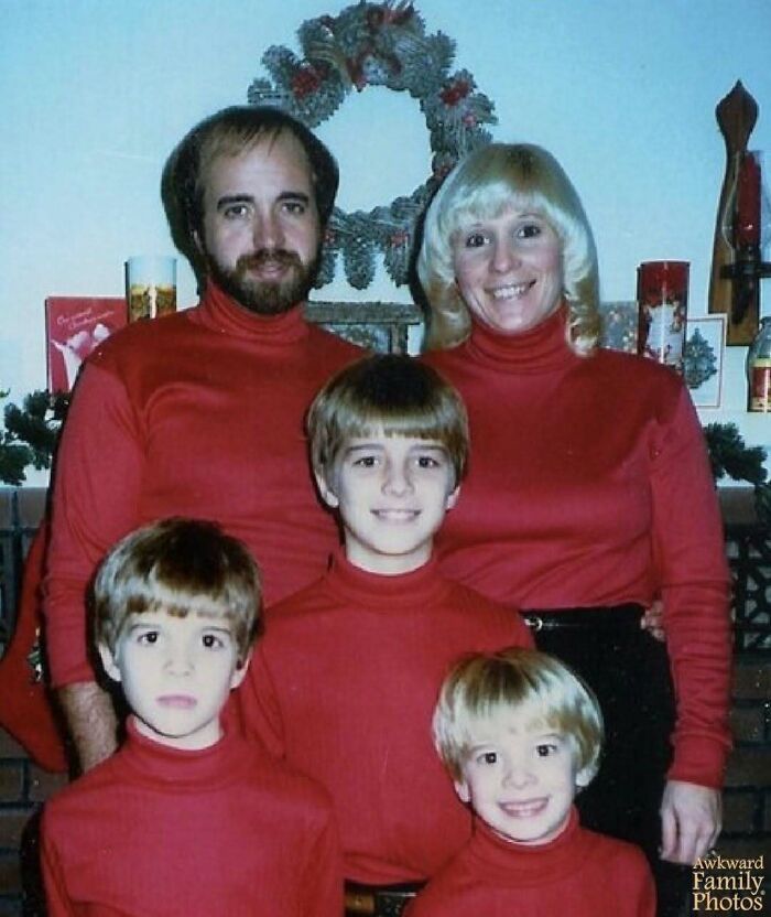 Family wearing matching red turtlenecks posing for awkward family Christmas photo with holiday decorations in background.