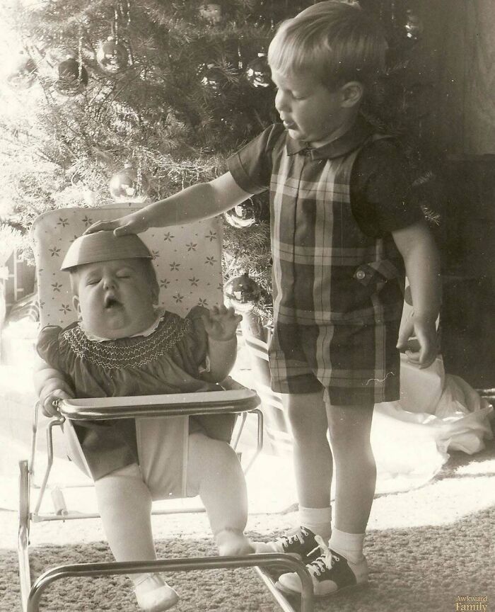 Black and white photo of two children by a Christmas tree in a hilariously awkward family Christmas moment.