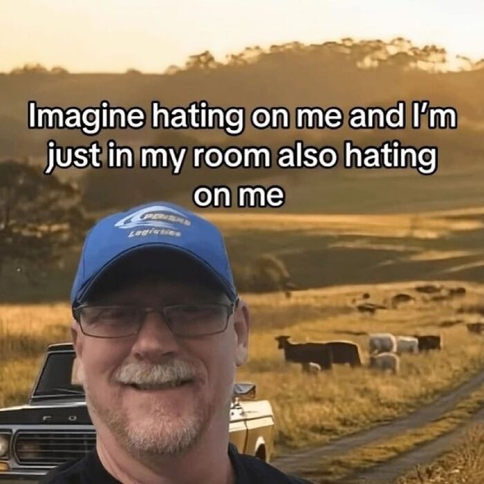 Man wearing a blue cap and glasses smiling in a field with cows, funny unhinged meme about self-hate.