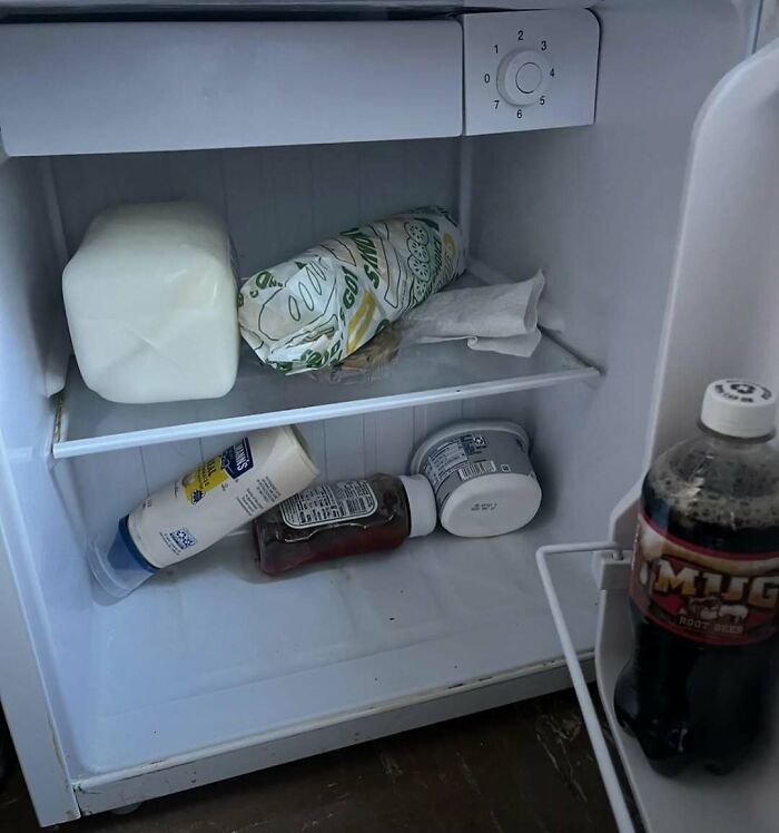 Small dude fridge with a few basic items including milk, sandwich, condiments, and a bottle of root beer inside.