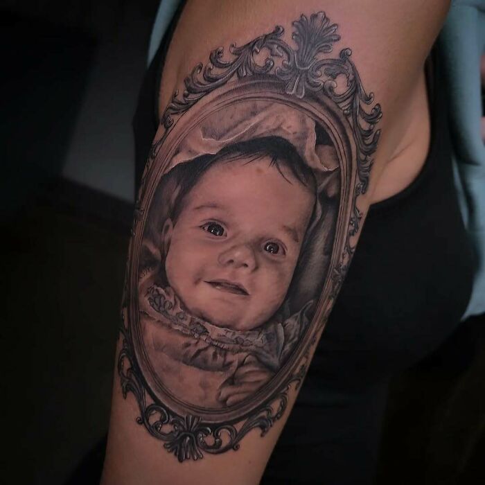 Realistic portrait tattoo of a baby framed in ornate vintage style, showcasing wholesome tattoos with meaningful ink on upper arm.