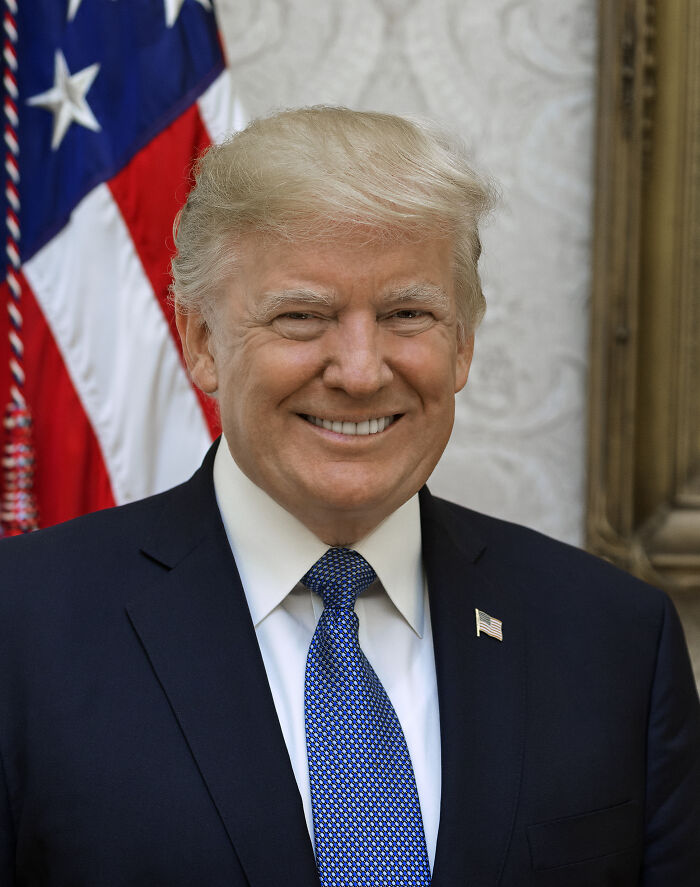Portrait of a suited man smiling in front of an American flag, representing one of the most disliked stars this year.