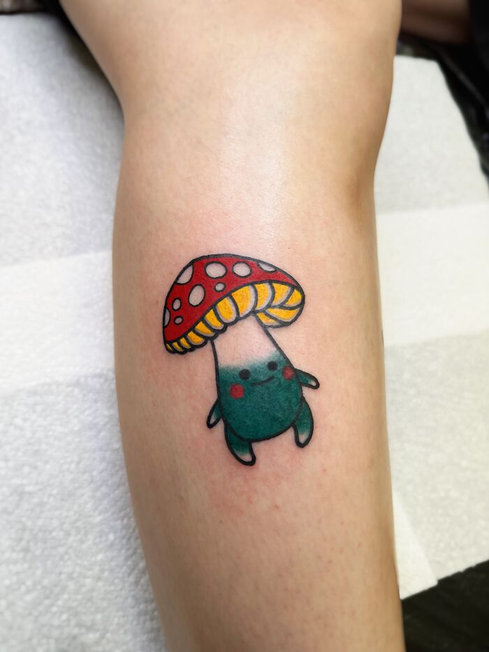 Colorful psychedelic tattoo of a whimsical mushroom character on a person's forearm attracting attention with its vibrant design.
