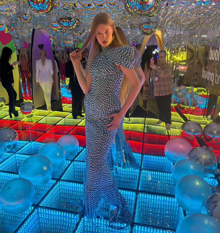 Young woman posing on colorful LED floor surrounded by reflective balloons in a mirrored room, evoking tragic mental illness theme.