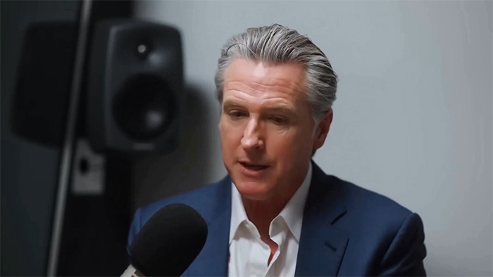 Man in navy suit speaking into microphone during a podcast, discussing tragic mental illness and public reaction online.