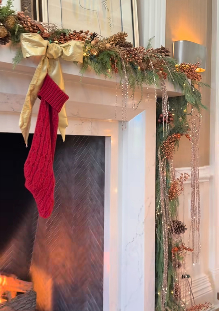Christmas fireplace decorated with garland, pinecones, and a red stocking, highlighting odd detail in Jennifer Lopez’s photo.
