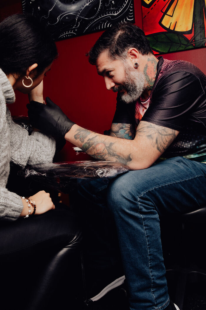 Tattoo artist with sleeve tattoos and gloves working on a client in an intimate studio recalling wild experiences.