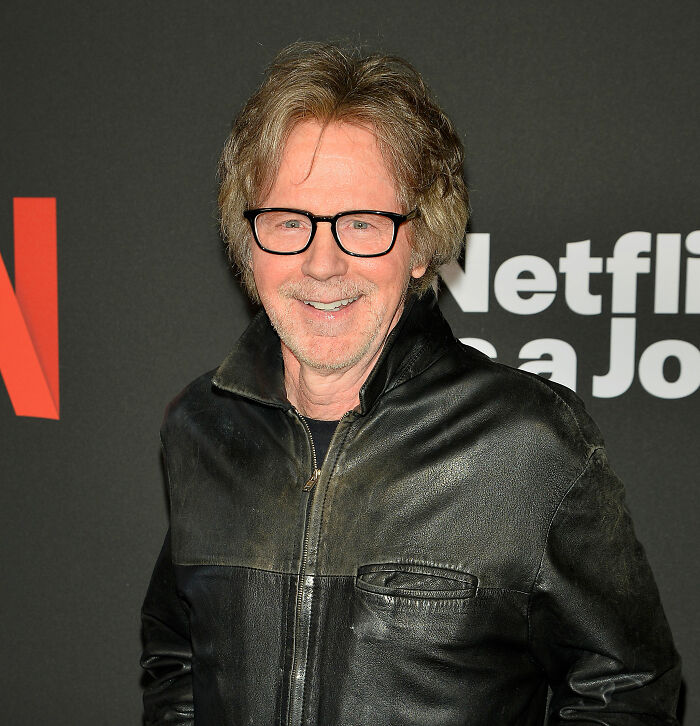 Man with glasses in a black leather jacket smiling at a Netflix event, related to banned stars from the Tonight Show topic.