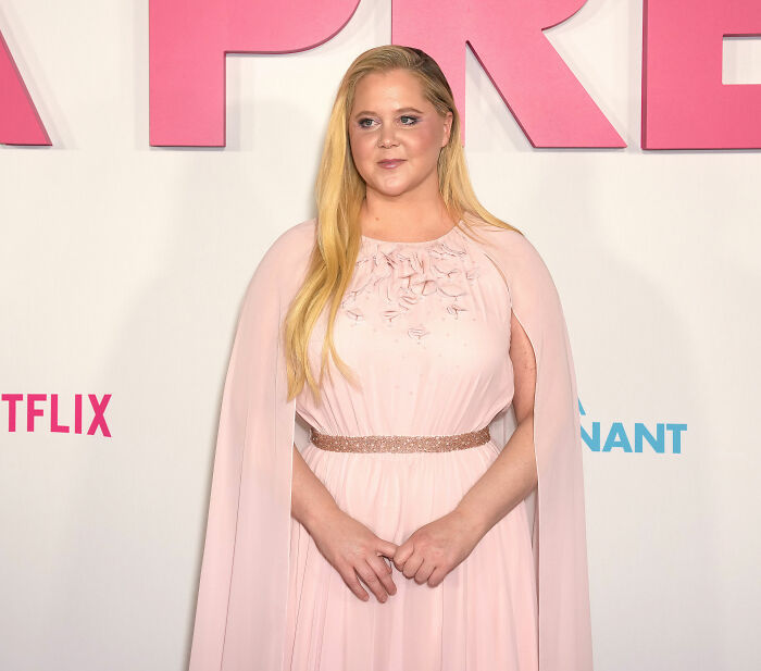 Amy Schumer posing in a pink dress at a Netflix event, showcasing dramatic weight loss and a confident look.
