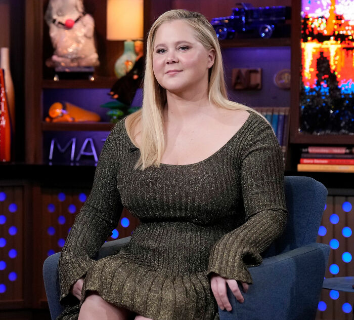 Amy Schumer seated indoors wearing a shimmery green dress, showing off dramatic weight loss during a TV interview.