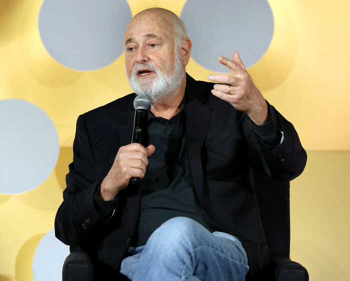 Rob Reiner speaking into a microphone, wearing a black jacket and jeans, discussing Donald Trump and hateful vile comments.
