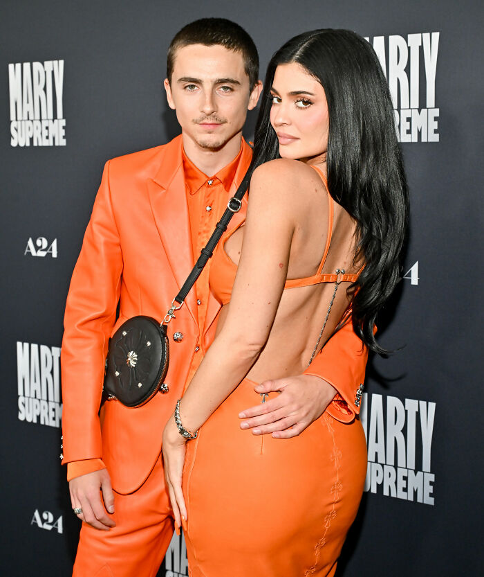 Timoth&eacute;e Chalamet and Kylie Jenner posing together on red carpet, both wearing coordinated orange outfits.