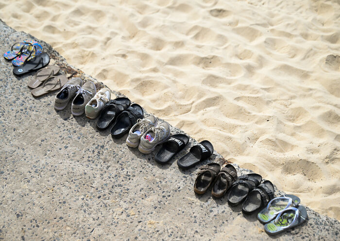 Various sandals and shoes neatly lined up along the edge of sandy beach, related to Bondi Beach attack GoFundMe controversy.