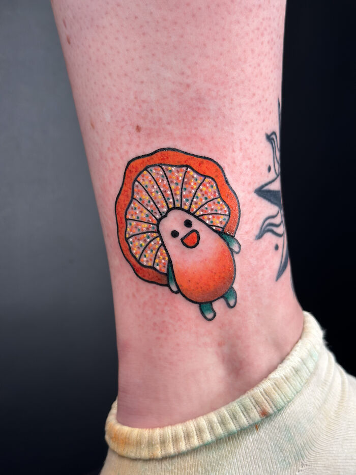 Psychedelic tattoo of a colorful smiling mushroom on ankle with vivid orange and green hues and decorative patterns.