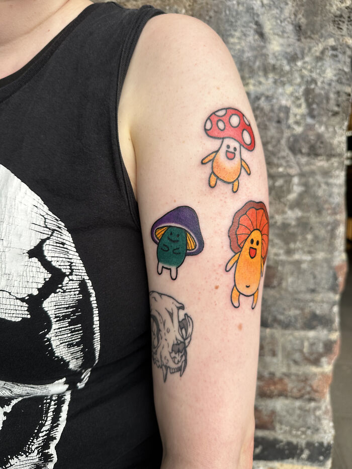 Colorful psychedelic tattoos of smiling mushrooms on a person's upper arm showcasing unique vibrant designs.