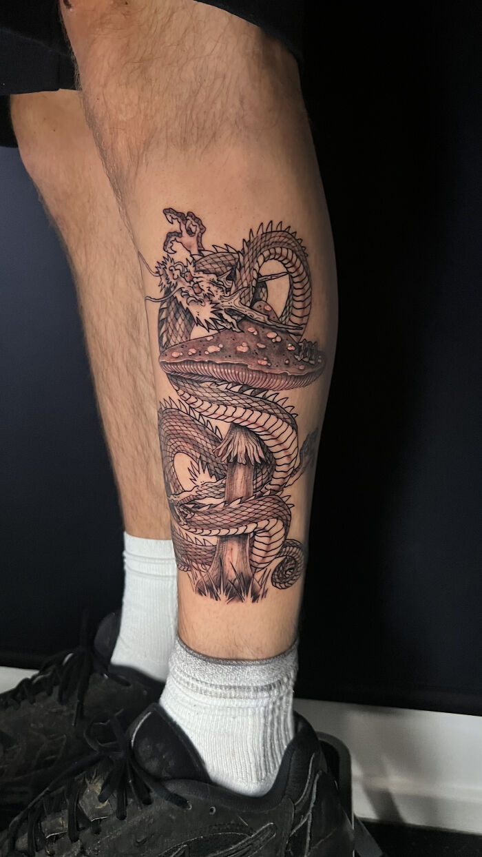 Tattoo of a detailed psychedelic dragon wrapped around a mushroom, showcasing unique psychedelic tattoo art on a leg.