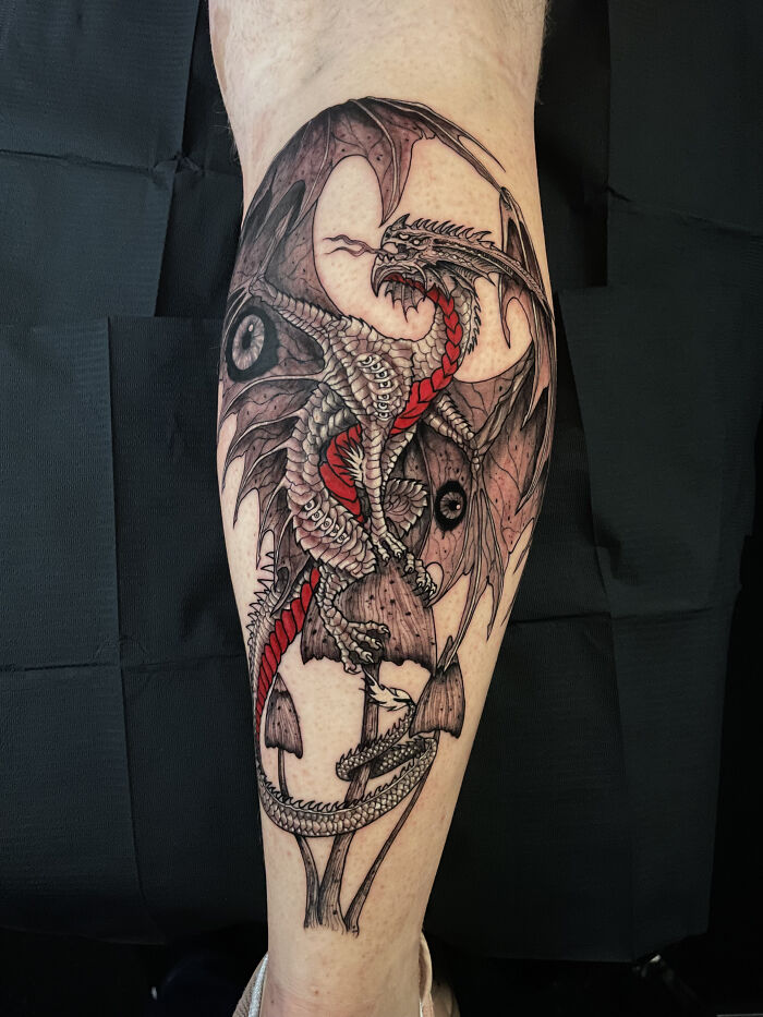 Psychedelic tattoo of a detailed dragon with red accents wrapped around mushrooms on a person&rsquo;s leg.