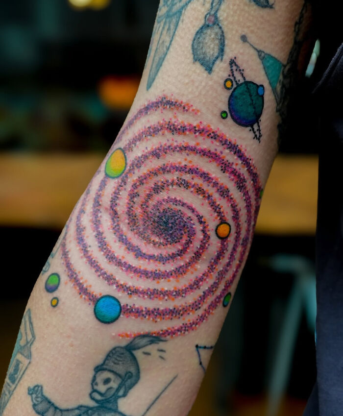 Colorful psychedelic tattoo featuring a spiral and planets on a forearm, showcasing unique and eye-catching tattoo art.