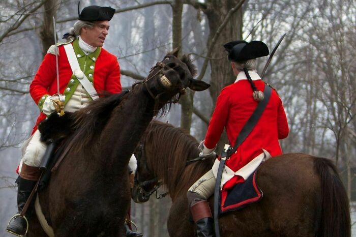 Two men in historical red uniforms on horses, with one horse making a funny face, a perfect timed funny pic.