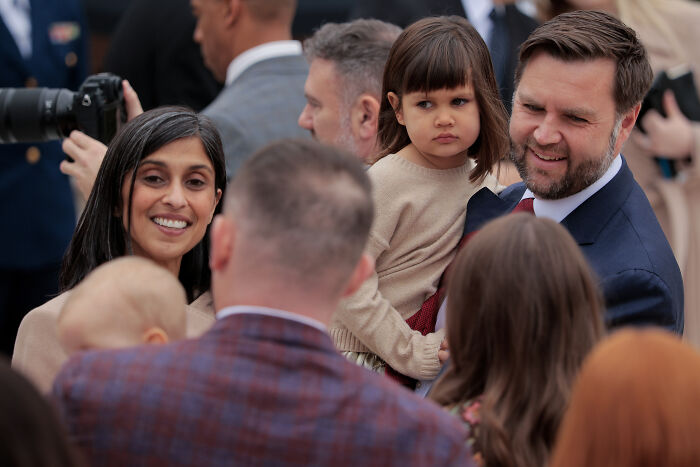 JD Vance smiling and holding a child, surrounded by people amid marriage speculation and viral hug discussions.
