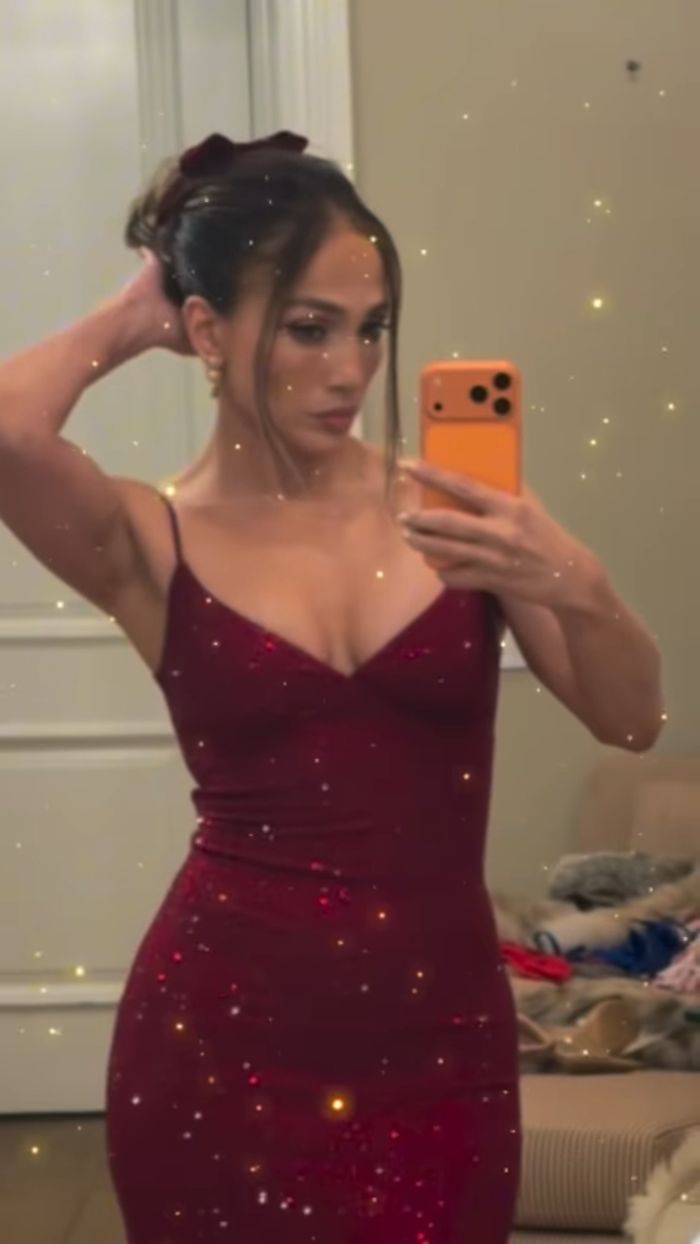 Jennifer Lopez taking a mirror selfie in a red dress with an odd detail sparking Photoshop skills discussion.