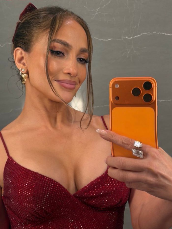 Jennifer Lopez taking a selfie in a red dress with an orange phone case, highlighting odd detail and Photoshop skills.