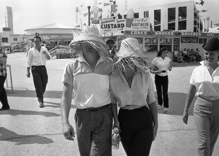 Couple wearing straw hats walking at a vintage fair, capturing a rarely-seen pop culture moment in black and white.