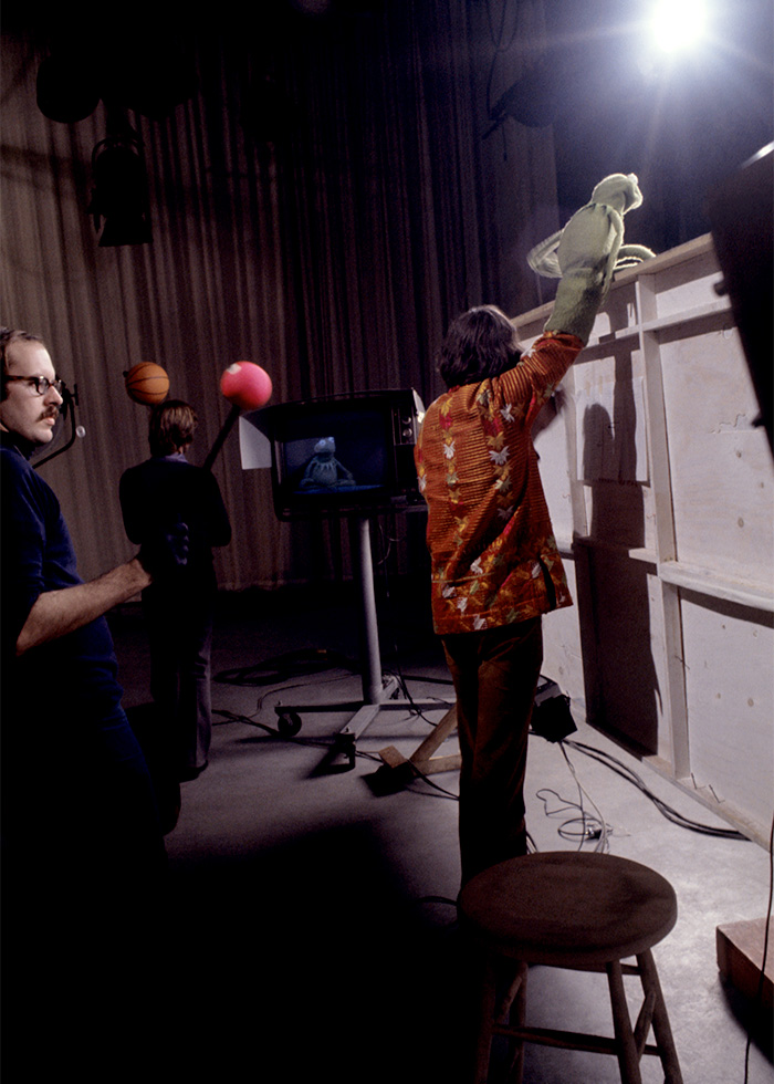 Behind-the-scenes pop culture shot of a puppeteer operating Kermit the Frog during a studio recording session.