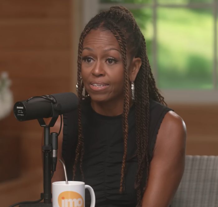 Michelle Obama speaking into a microphone during an interview, showcasing her bold new makeup look.