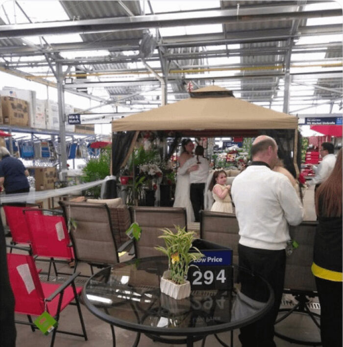 Walmart store interior with patio furniture display including table, chairs, canopy, and people browsing unusual items.