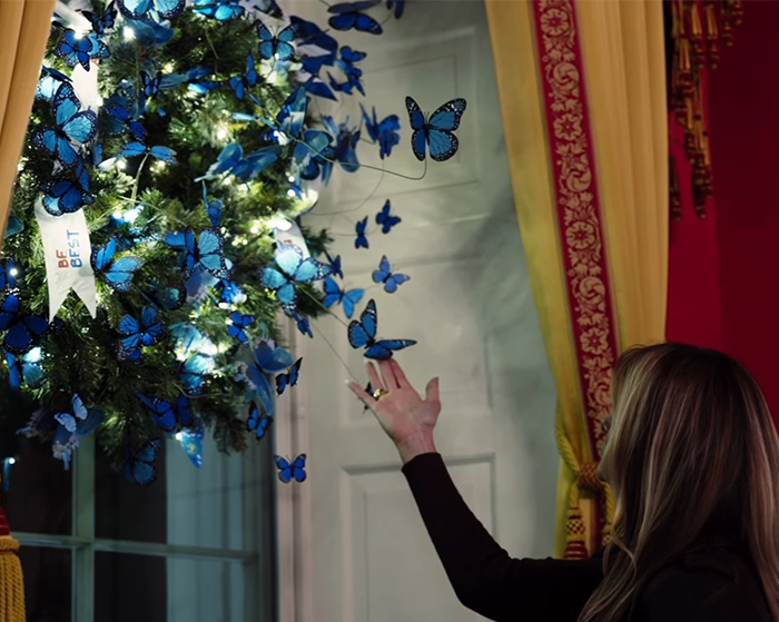 Woman reaching toward a Christmas ornament with blue butterflies, linked to Melania Trump's new Christmas ornament controversy.