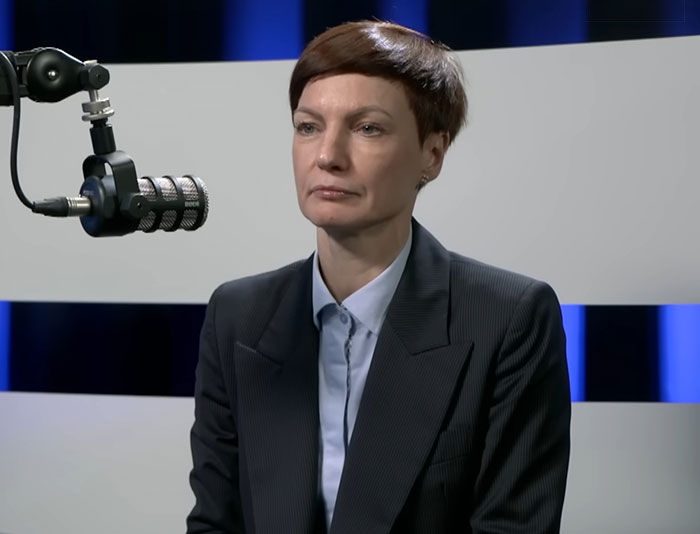 Person in a dark suit speaking into a microphone during an interview about Lithuania lawmaker&rsquo;s cat consent for broadcaster firing.