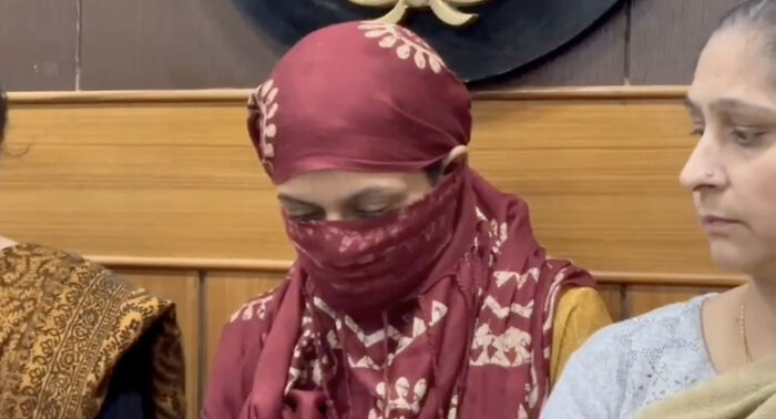 Woman wearing maroon headscarf and face covering sitting beside another woman in emotional setting revealing wedding tragedy pattern.