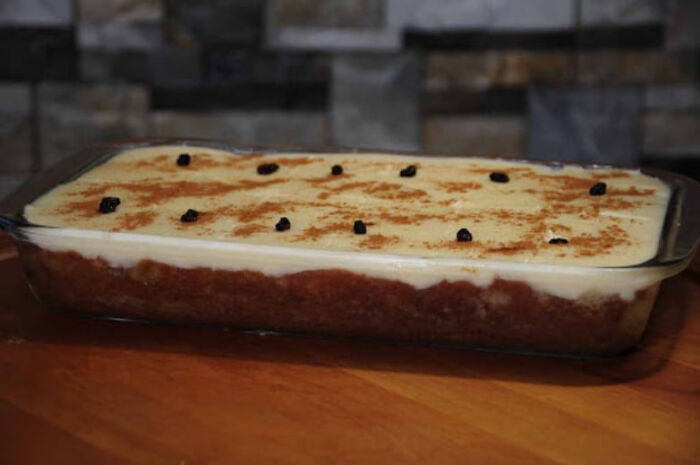 Christmas dessert in a clear glass dish topped with creamy layer, cinnamon, and small dark dried fruit pieces.