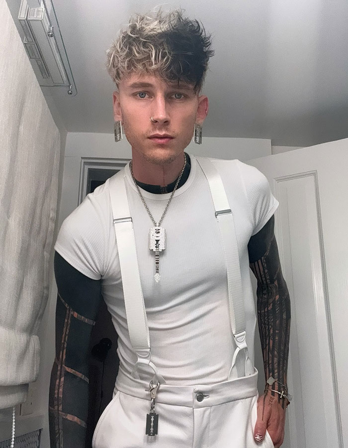 Machine Gun Kelly posing indoors wearing white suspenders and jewelry, related to boy band dancing viral reaction. Machine Gun Kelly posing indoors wearing white suspenders and jewelry, related to boy band dancing viral reaction.