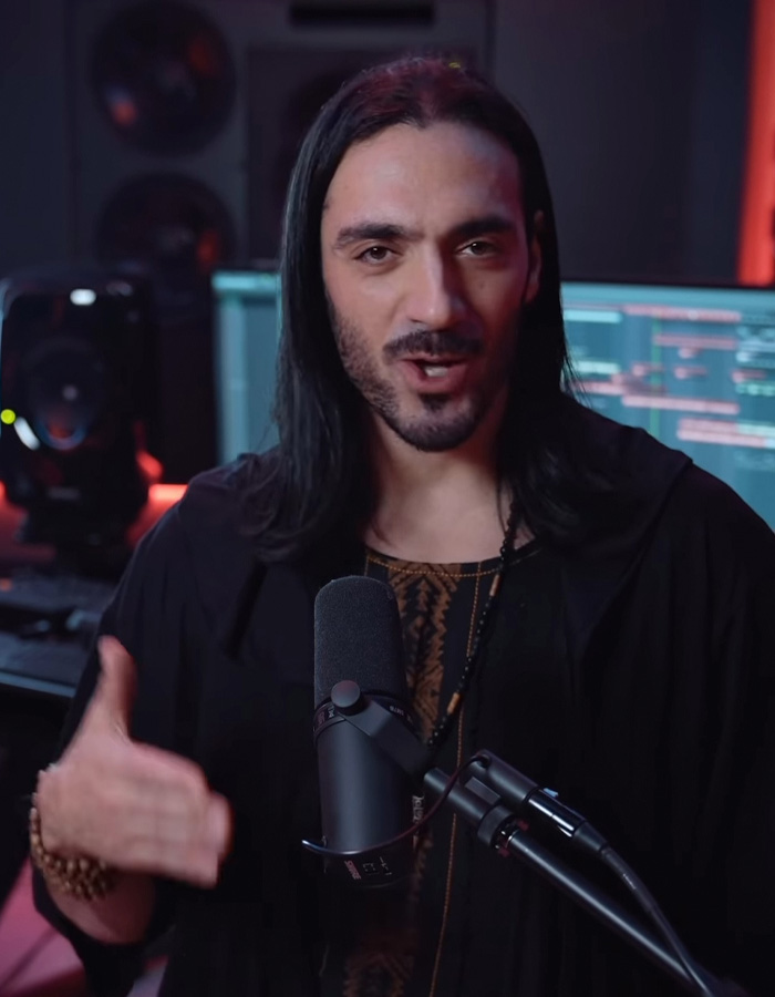 Man with long hair performing Mongolian jingle bells throat singing in a recording studio with microphone and audio equipment.