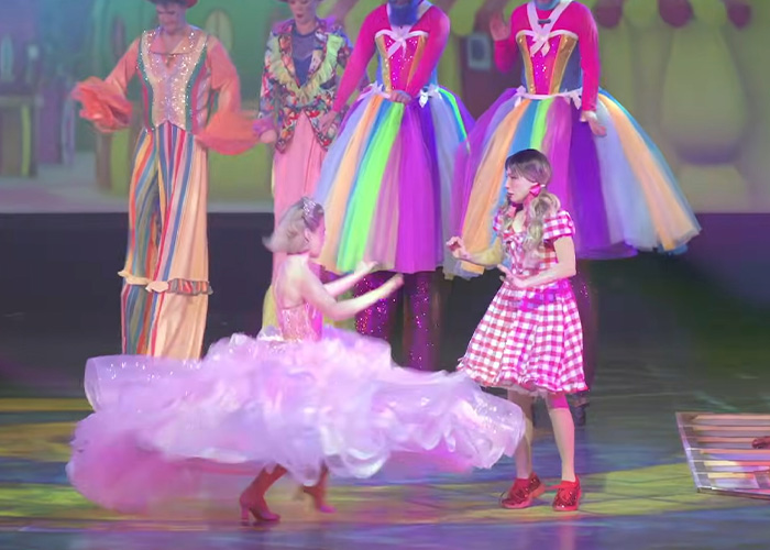 Actors in colorful costumes performing a Wizard Of Oz stage show with vibrant dresses and lively action on stage.