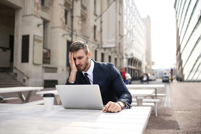 Man in a suit looking stressed while using a laptop outdoors, reflecting on staying calm or losing it scenarios.