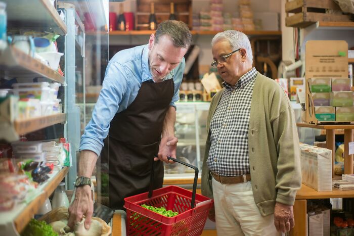 Man wearing apron helping elderly customer in grocery store, illustrating staying calm in everyday scenarios.