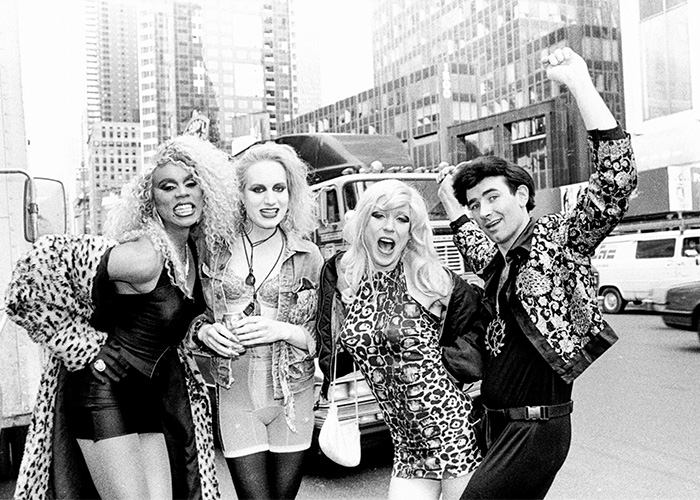 Group of four people dressed in 80s style outside in city, showcasing rare pop culture shots with energetic poses and fashion.