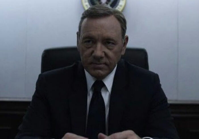 Man in dark suit and tie sitting at a desk with a serious expression referencing Harvey Weinstein controversy. Man in dark suit and tie sitting at a desk with a serious expression referencing Harvey Weinstein controversy.