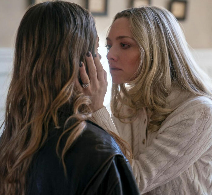 Two women in an intense moment indoors, with one gently holding the other's face in a dramatic scene.