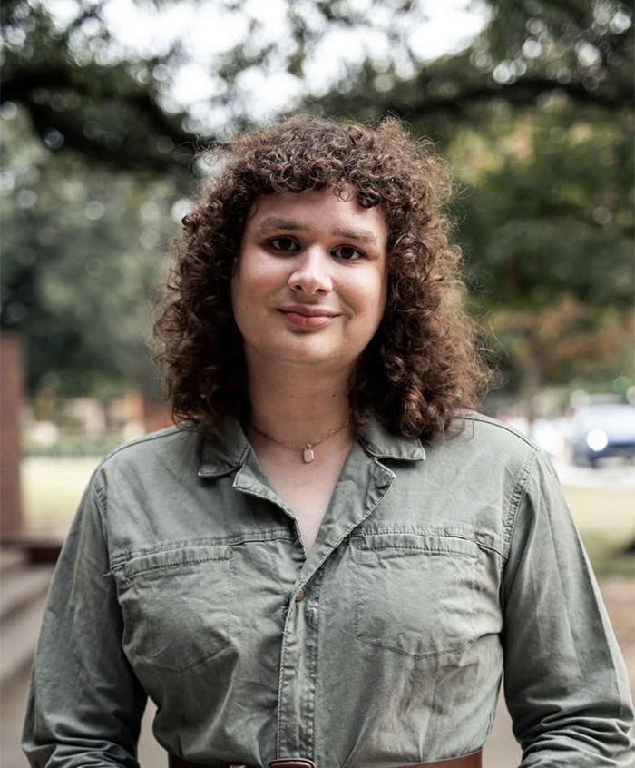 Young student outdoors with curly hair and green shirt, symbolizing essay that got trans instructor removed from university.